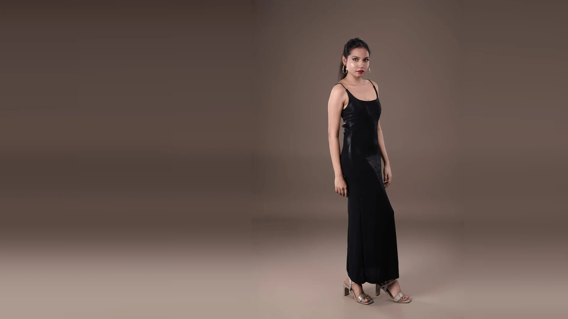 Full-length fashion portrait in a black dress against a warm studio backdrop