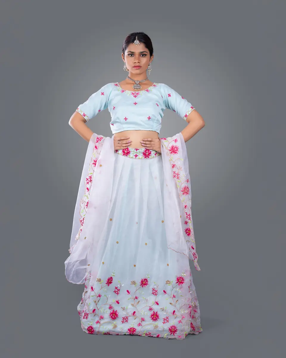 Full-length fashion portrait in a pale blue floral lehenga against a grey studio backdrop
